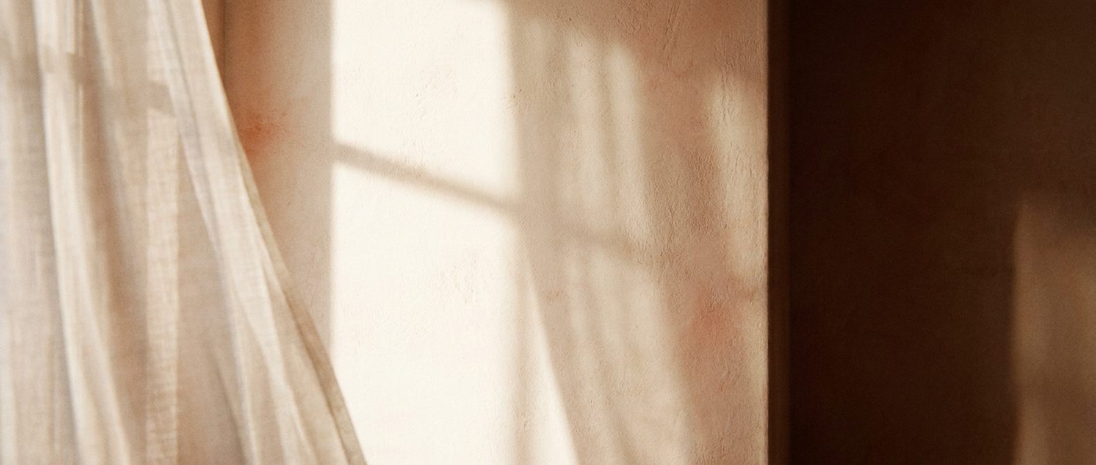 Morning light through a sheer curtain, falling across a warm cream wall
