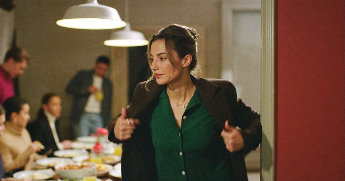How to set boundaries with family: a woman puts on her coat to leave a family dinner early, calm and decided, relatives talking behind her